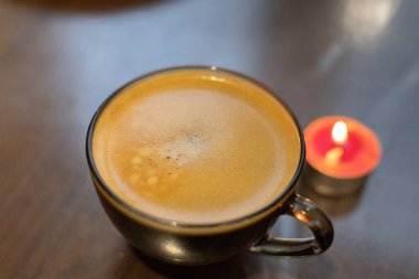 Şeffaf bir fincanda kahve ve yakınlarda yanan bir mum. Elektriksel sorunlar nedeniyle karartma