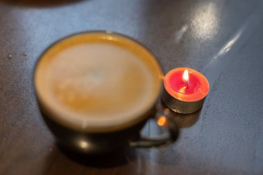 Şeffaf bir fincanda kahve ve yakınlarda yanan bir mum. Elektriksel sorunlar nedeniyle karartma