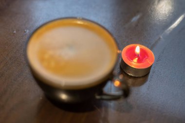 Şeffaf bir fincanda kahve ve yakınlarda yanan bir mum. Elektriksel sorunlar nedeniyle karartma