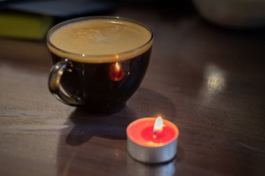 Şeffaf bir fincanda kahve ve yakınlarda yanan bir mum. Elektriksel sorunlar nedeniyle karartma
