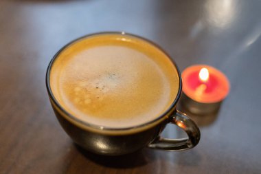 Şeffaf bir fincanda kahve ve yakınlarda yanan bir mum. Elektriksel sorunlar nedeniyle karartma