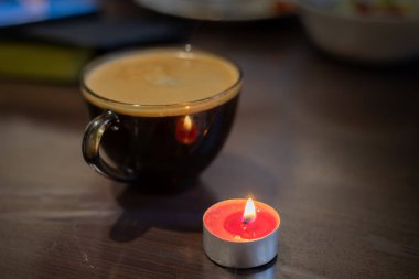 Şeffaf bir fincanda kahve ve yakınlarda yanan bir mum. Elektriksel sorunlar nedeniyle karartma
