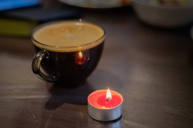 Şeffaf bir fincanda kahve ve yakınlarda yanan bir mum. Elektriksel sorunlar nedeniyle karartma