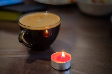 Şeffaf bir fincanda kahve ve yakınlarda yanan bir mum. Elektriksel sorunlar nedeniyle karartma