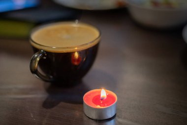 Şeffaf bir fincanda kahve ve yakınlarda yanan bir mum. Elektriksel sorunlar nedeniyle karartma