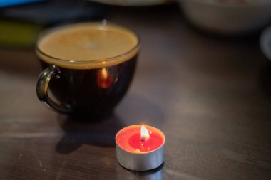 Şeffaf bir fincanda kahve ve yakınlarda yanan bir mum. Elektriksel sorunlar nedeniyle karartma