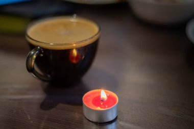 Şeffaf bir fincanda kahve ve yakınlarda yanan bir mum. Elektriksel sorunlar nedeniyle karartma