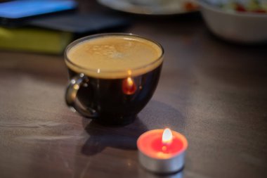 Şeffaf bir fincanda kahve ve yakınlarda yanan bir mum. Elektriksel sorunlar nedeniyle karartma