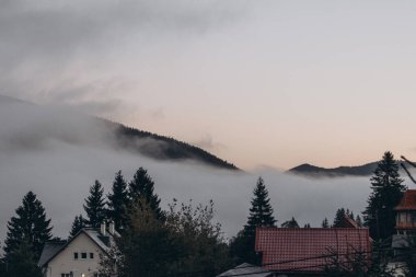 Dağ ormanlarına ve evlere bakan manzaralı bir manzara. Dağlarda şafak vakti. Sis kırsal kesimi kaplıyor. Pankart arkaplan, duvar kağıdı olarak kullanılabilir