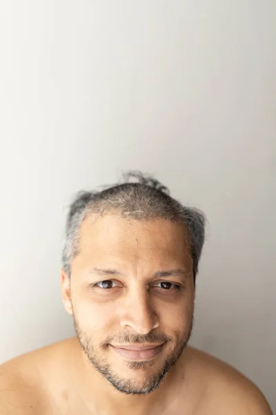 Handsome gray-haired man is cutting hair himself with an electric hair clipper.