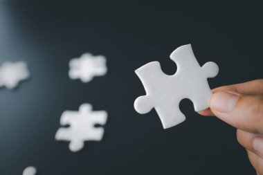 El ele yapboz, iş ortaklığı konsepti. İş adamlarının elleri yapboz parçalarını karanlık arka planda birbirine bağlar. İş konsepti, takım çalışması, işbirliği, ortaklık, yaratıcı.