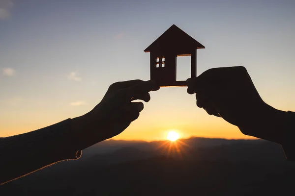silhouette of male and female hands holding model house at sunset Concept of buying houses, real estate.