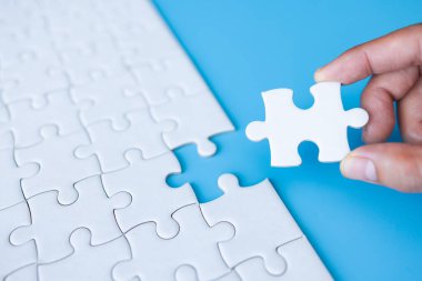 Hand put last piece of jigsaw puzzle. White unfinished jigsaw puzzle on  blue background.The correct solution. Teamwork, Solving and completing the task. Assembling jigsaw puzzle pieces.
