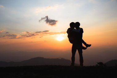Silhouette of a couple on the mountain, A young romantic couple enjoy a beautiful view of the sun setting over the mountains, love, Valentine's Day.
