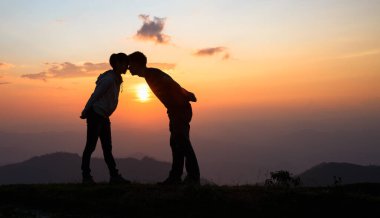 Silhouette of a couple on the mountain, A young romantic couple enjoy a beautiful view of the sun setting over the mountains, love, Valentine's Day.