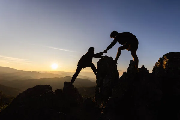 Silhouette Teamwork, Male hikers climbing up mountain cliff and one of them giving helping hand. People helping and, team work concept.