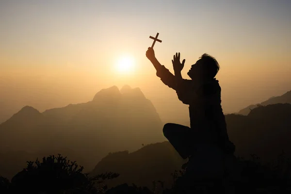 祈りと精神性のための概念として日没時にキリスト教の十字架で祈る忠実な男のシルエット — ストック写真