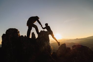 silhouette of Teamwork of two men hiker helping each other on top of mountain climbing team. Teamwork friendship hiking help each other trust assistance silhouette in mountains, sunrise. 