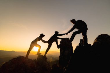 Yürüyüşçülerin silueti dağ yamacına tırmanıyor. Gün batımında tırmanırken birbirlerine yardım eden bir grup. Yardım ve takım çalışması kavramı.