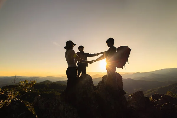 stock image Silhouette of celebrating life, Hikers climbing up mountain cliff. Businessman and women group hike on the peak of  rocks mountain at sunset, success, winner and leader concept.