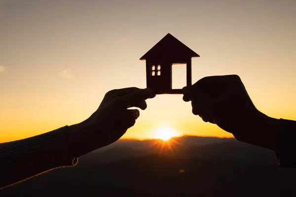 stock image silhouette of male and female hands holding model house at sunset Concept of buying houses, real estate.