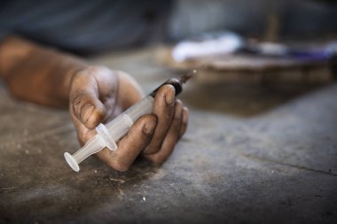 Bir uyuşturucu bağımlısının insan eli ve yerde yatan bir şırınga. Uyuşturucu karşıtı. Erkek uyuşturucu bağımlısı, uyuşturucu şırıngası.