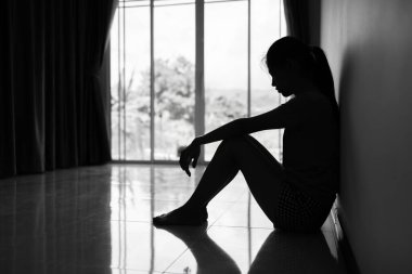 Silhouette of Depressed young woman near window at home, closeup in the dark room. domestic violence, violence against womenBlack and white photo.