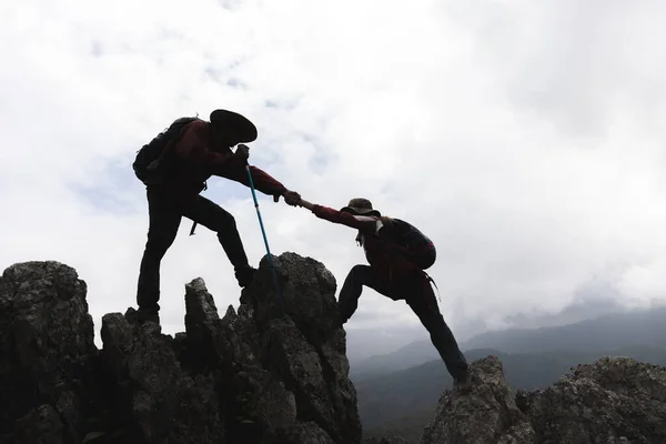 Silhouette of Two male  hikers climbing up mountain cliff and one of them giving helping hand. People helping and, team work concept.