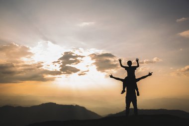 Gün batımının ortasında babasının boynunda gezen bir çocuğun silueti Mutlu bayram konsepti Mutlu aile.