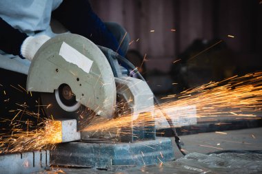 Heavy Industry Engineering Factory Interior with Industrial Worker Using Angle Grinder and Cutting a Metal Tube. Metal ve çeliği keskin yuvarlak bir bıçakla dairesel testereyle kesiyor..