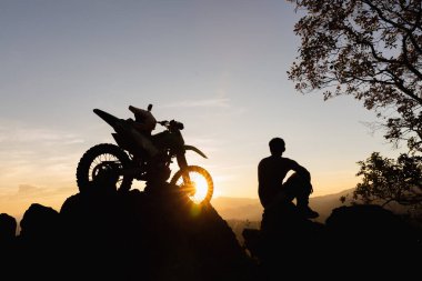Motosikletli bir adam güzel ışıklara karşı, motosikletli bir adamın silüeti kayanın tepesinde, gün batımında, dayanıklı motosiklet yolculuğu konsepti..