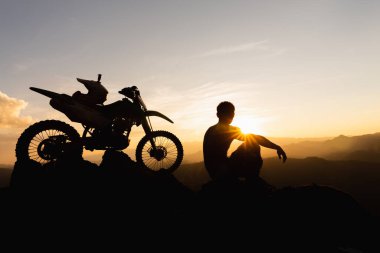 Motosikletli bir adam güzel ışıklara karşı, motosikletli bir adamın silüeti kayanın tepesinde, gün batımında, dayanıklı motosiklet yolculuğu konsepti..