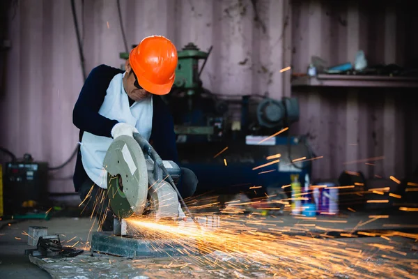 Heavy Industry Engineering Factory Interior with Industrial Worker Using Angle Grinder and Cutting a Metal Tube. Cutting metal and steel with a combination circular saw with a sharp round blade.