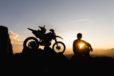 Motosikletli bir adam güzel ışıklara karşı, motosikletli bir adamın silüeti kayanın tepesinde, gün batımında, dayanıklı motosiklet yolculuğu konsepti..
