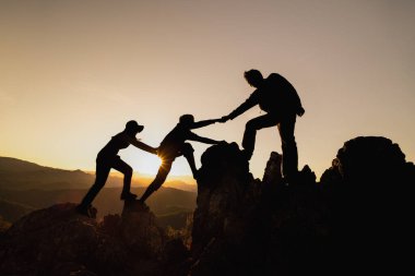 silhouette of Teamwork of three  hiker helping each other on top of mountain climbing team. Teamwork friendship hiking help each other trust assistance silhouette in mountains, sunrise. 