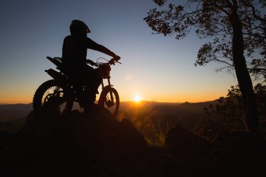 Motosikletli bir adam güzel ışıklara karşı, motosikletli bir adamın silüeti kayanın tepesinde, gün batımında, dayanıklı motosiklet yolculuğu konsepti..