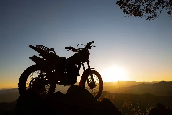 motocross bike against beautiful lights, silhouette of a  motocross motorcycle On top of rock high mountain at beautiful sunset, enduro motorcycle travel concept.