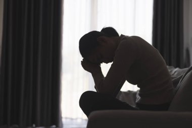 Evde depresyondan muzdarip bir insanın silueti koltukta yalnız başına oturan depresyonlu bir kadın karanlık odada üzgün ve endişeli hissediyor. İnsan streslidir..
