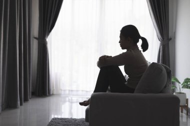Evde depresyondan muzdarip bir insanın silueti koltukta yalnız başına oturan depresyonlu bir kadın karanlık odada üzgün ve endişeli hissediyor. İnsan streslidir..