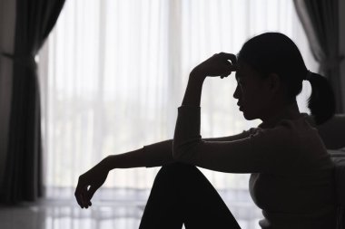 Evde depresyondan muzdarip bir insanın silueti koltukta yalnız başına oturan depresyonlu bir kadın karanlık odada üzgün ve endişeli hissediyor. İnsan streslidir..