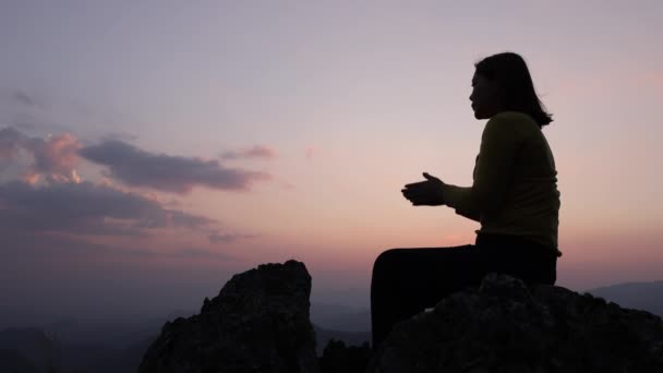 一个女人双手紧握在一起坐在岩石上 慢慢张开手掌许愿的轮廓 信仰和信念 — 图库视频影像
