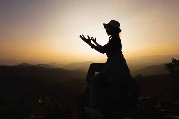 Silhouette of a women is praying to God on the mountain. Praying hands with faith in religion and belief in God on blessing background. Power of hope or love and devotion.