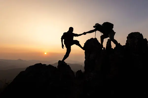 person on top of mountain. silhouette of people team hiking to top of mountain in sunset, climbing team success on the mountain. Leadership Concept, teamwork.