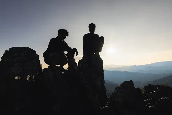 person on top of mountain, Silhouette of Young people sitting on a rock  looking to the horizon.
