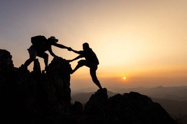 silhouette of Teamwork of two men hiker helping each other on top of mountain climbing team. Teamwork friendship hiking help each other trust assistance silhouette in mountains, sunrise. 