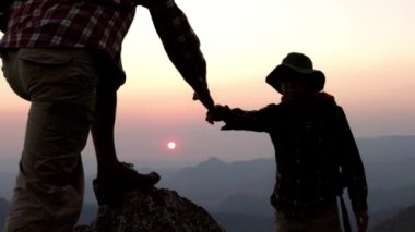 Gün doğumunda bir dağa tırmanırken birbirine yardım eden insanların silueti. Yardım eli uzatmak, ve aktif ve sağlıklı yaşam tarzı kavramı. yardım ve başarı kavramı, liderlik kavramı, konsept, takım çalışması.
