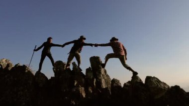 Grup turistlerinin silueti uçurumlara tırmanmaya yardım ediyor. Takım çalışması dağcılar zorlukların üstesinden gelir, takım çalışması elle seyahat kavramına yardımcı olur.