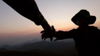 Yürüyüşçülerin silueti dağ yamacına tırmanıyor. Gün batımında tırmanırken birbirlerine yardım eden bir grup. Yardım ve takım çalışması kavramı.