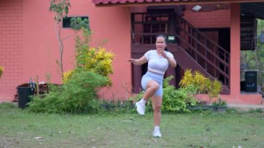 Orta yaşlı bir kadın evinin önündeki çimlerde egzersiz yapıyor..