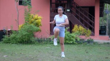 Orta yaşlı bir kadın evinin önündeki çimlerde egzersiz yapıyor..